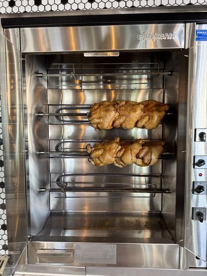Zwei Reihen Hähnchen auf Drehspießen im geöffneten Edelstahlgrill